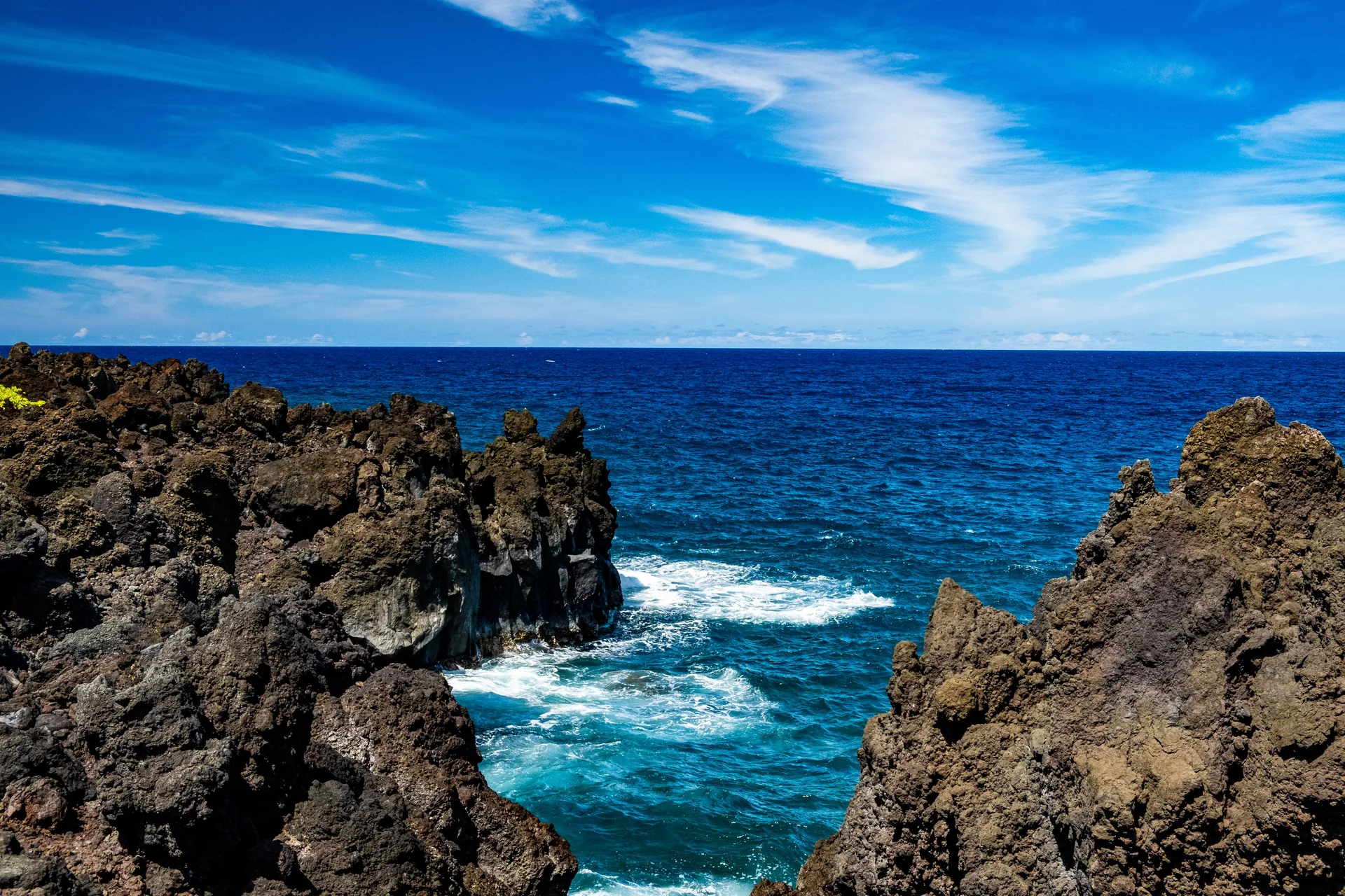 Littoral volcanique escarpé bordé d'une eau turquoise, sous un ciel dégagé